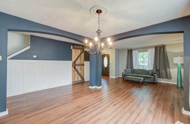 unfurnished dining area with hardwood / wood-style floors, a barn door, a textured ceiling, and a notable chandelier