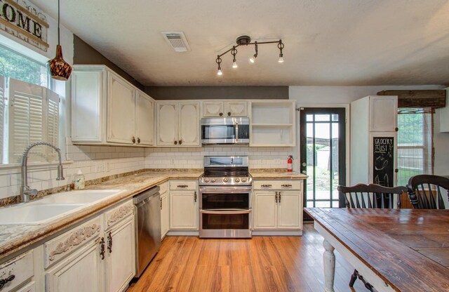 kitchen featuring sink, decorative backsplash, light wood-type flooring, appliances with stainless steel finishes, and decorative light fixtures