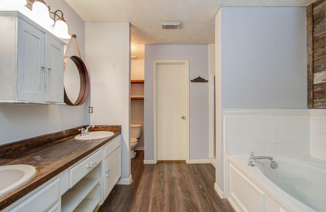 bathroom featuring a tub, wood-type flooring, a textured ceiling, toilet, and vanity