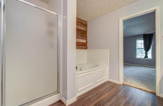 bathroom with shower with separate bathtub, a textured ceiling, hardwood / wood-style flooring, and wood walls