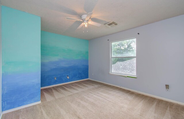 empty room with ceiling fan, light colored carpet, and a textured ceiling