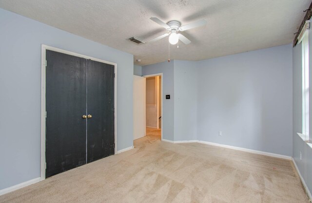 unfurnished bedroom featuring a textured ceiling, light colored carpet, a closet, and ceiling fan