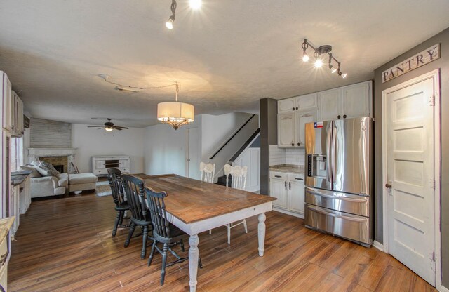 dining space featuring a textured ceiling, dark hardwood / wood-style flooring, a large fireplace, and ceiling fan with notable chandelier