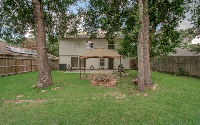 rear view of property featuring a gazebo, a yard, central AC unit, and an outdoor fire pit