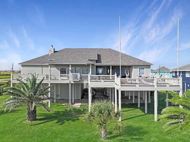 rear view of property featuring a shingled roof, a lawn, and a deck