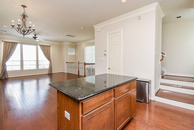 kitchen with pendant lighting, crown molding, dark stone countertops, dark hardwood / wood-style floors, and a center island