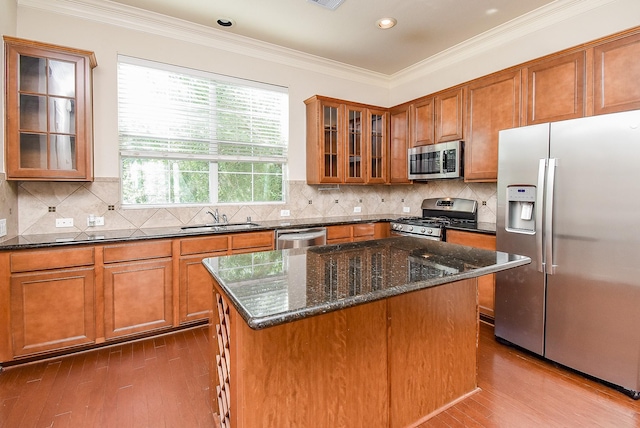 kitchen featuring a kitchen island, sink, dark stone counters, stainless steel appliances, and crown molding