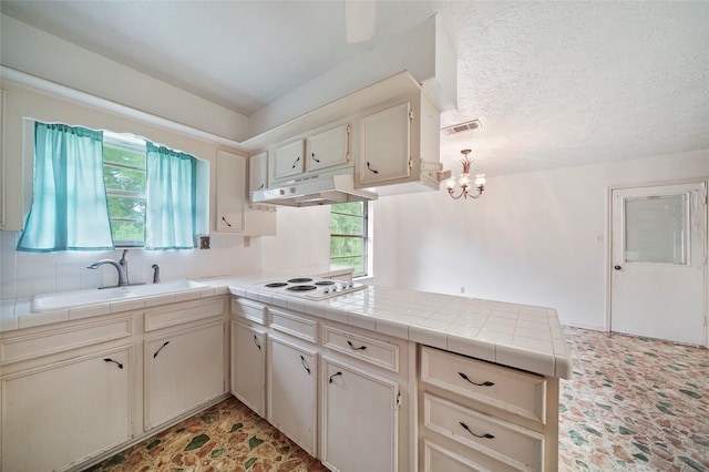 kitchen with sink, a textured ceiling, white electric stovetop, tile counters, and cream cabinetry