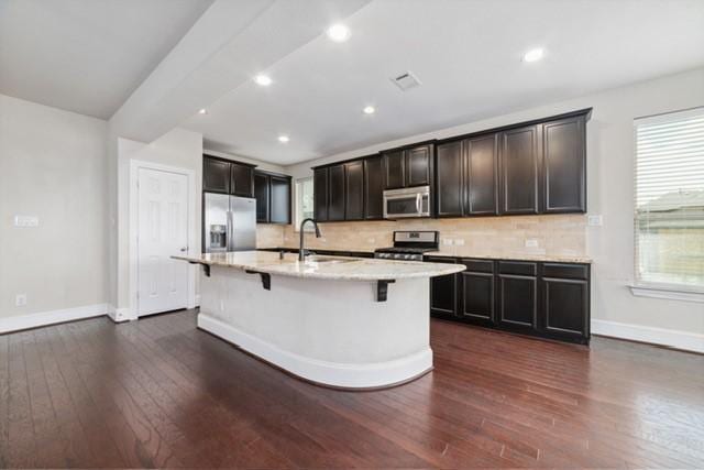 kitchen featuring sink, stainless steel appliances, dark hardwood / wood-style floors, an island with sink, and a kitchen bar