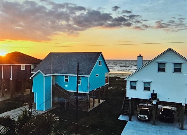 back house at dusk featuring a beach view and a water view