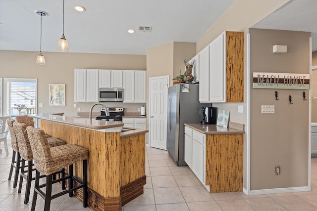 kitchen featuring stainless steel appliances, light tile patterned floors, an island with sink, pendant lighting, and white cabinets