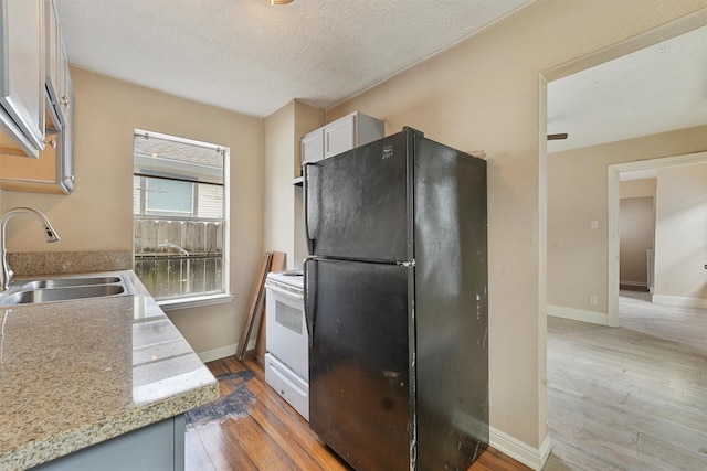 kitchen with white cabinetry, white range with electric cooktop, light wood-type flooring, black fridge, and sink