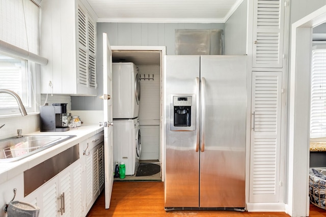 kitchen featuring stacked washer and dryer, crown molding, light hardwood / wood-style flooring, sink, and stainless steel refrigerator with ice dispenser