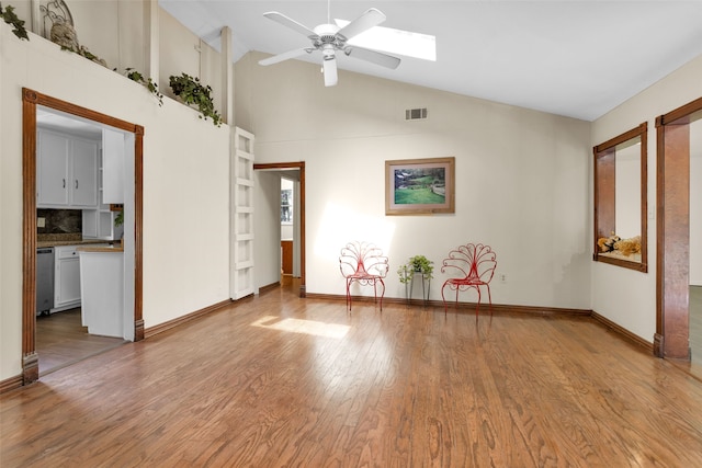 empty room featuring a skylight, high vaulted ceiling, light wood-type flooring, and ceiling fan