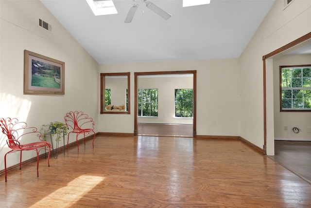 living area featuring lofted ceiling with skylight, light wood-type flooring, and ceiling fan