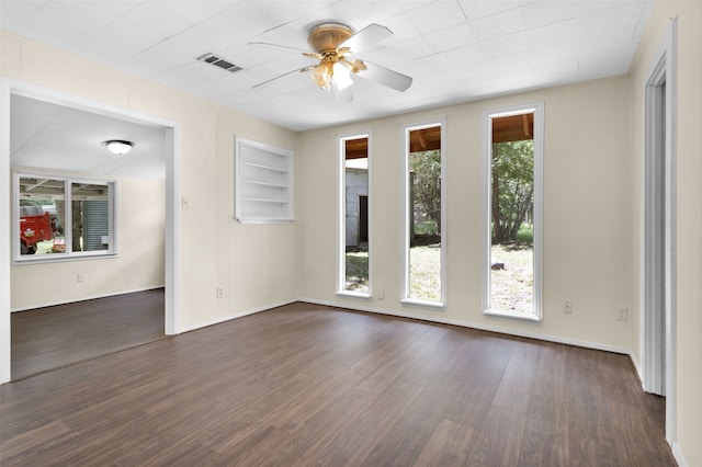 empty room with dark wood-type flooring, built in shelves, and ceiling fan