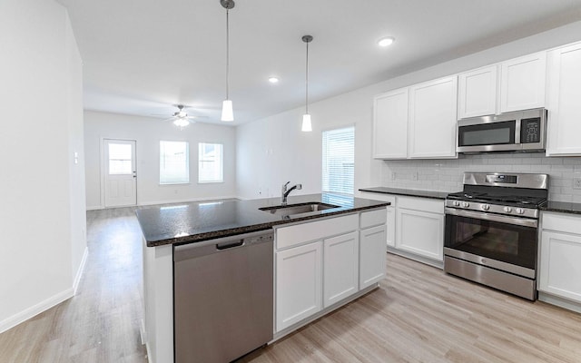 kitchen with a center island with sink, stainless steel appliances, decorative light fixtures, sink, and white cabinets