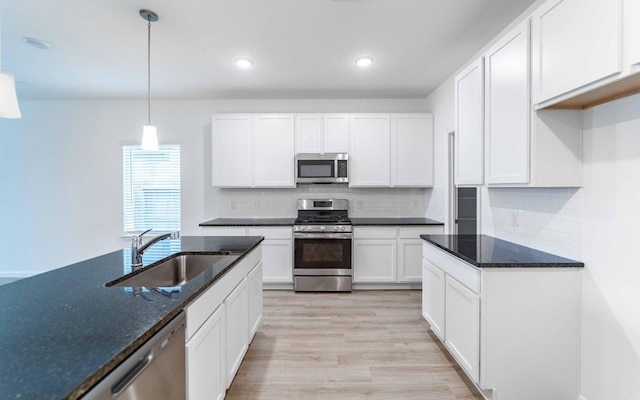 kitchen with dark stone countertops, sink, stainless steel appliances, white cabinets, and hanging light fixtures