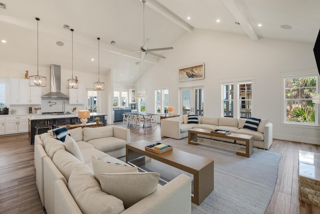 living room with beamed ceiling, high vaulted ceiling, ceiling fan with notable chandelier, and light wood-type flooring