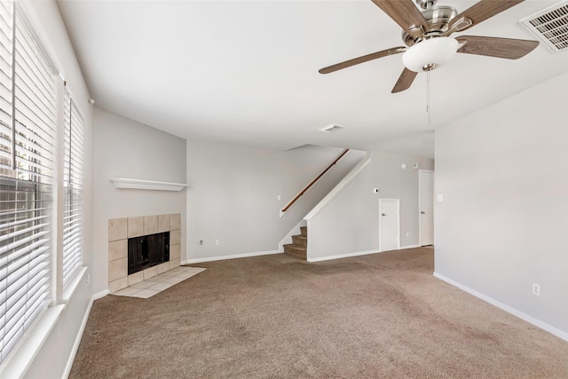 unfurnished living room with a tiled fireplace, light carpet, and ceiling fan