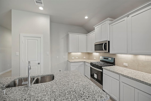 kitchen featuring stainless steel appliances, white cabinetry, light stone counters, and sink