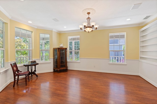 empty room featuring dark hardwood / wood-style flooring, built in features, crown molding, and an inviting chandelier