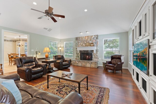 living room featuring ceiling fan with notable chandelier, dark hardwood / wood-style flooring, a stone fireplace, and vaulted ceiling