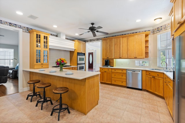 kitchen featuring a kitchen bar, stainless steel appliances, ceiling fan, sink, and a center island