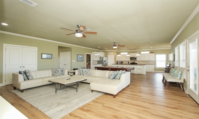 living room featuring ceiling fan, ornamental molding, and light wood-type flooring