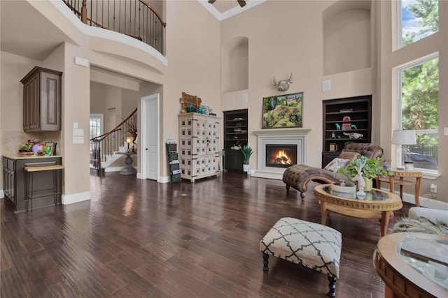 living room featuring stairs, baseboards, dark wood-type flooring, and a glass covered fireplace