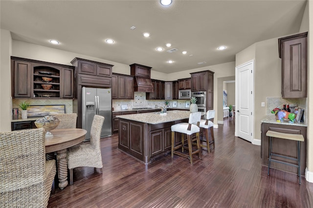 kitchen with decorative backsplash, dark brown cabinetry, stainless steel appliances, a kitchen island with sink, and dark hardwood / wood-style floors