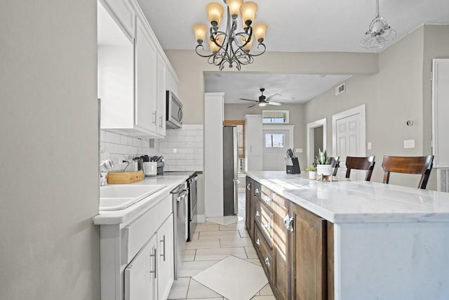 kitchen featuring white cabinets, ceiling fan with notable chandelier, decorative backsplash, a kitchen island, and stainless steel appliances