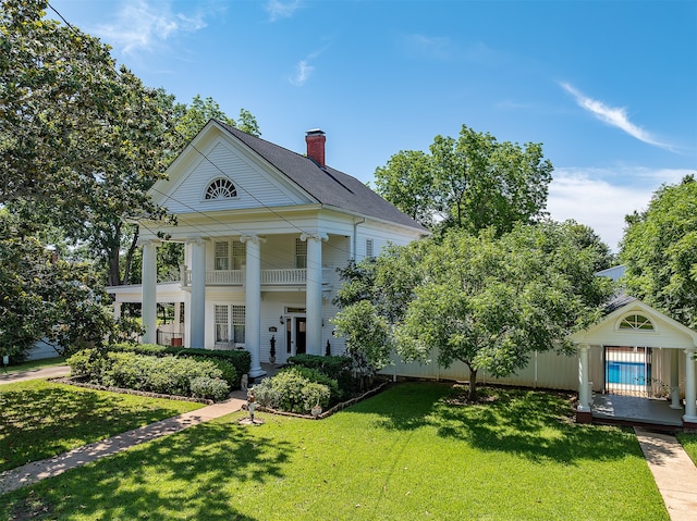 greek revival inspired property with ceiling fan, a balcony, and a front yard