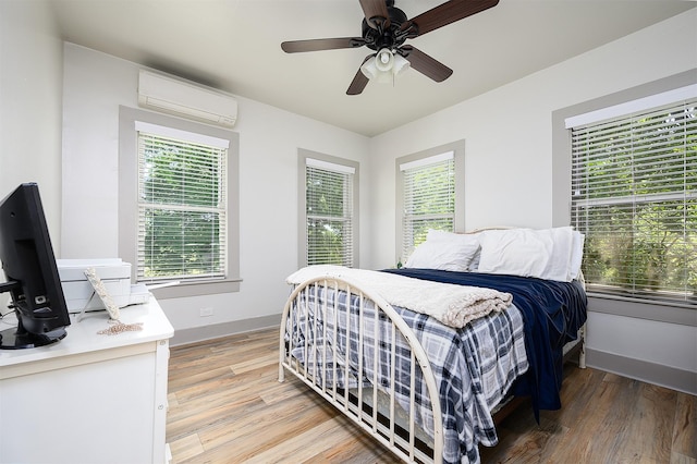 bedroom featuring light wood-style floors, an AC wall unit, multiple windows, and baseboards