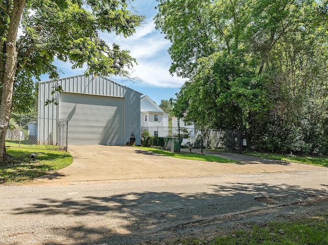 exterior space featuring driveway, a detached garage, fence, and an outbuilding