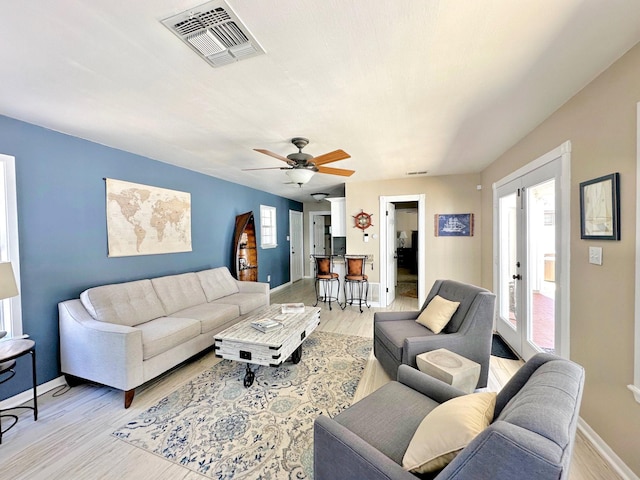 living room featuring ceiling fan, light wood-type flooring, visible vents, and baseboards