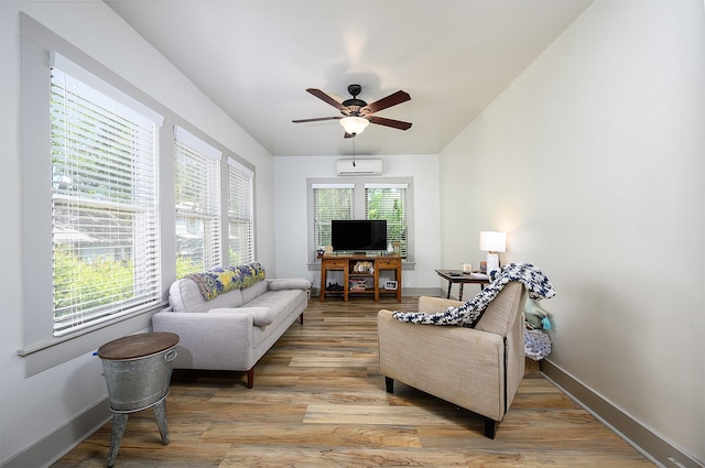 living area featuring ceiling fan, light wood-type flooring, a wall unit AC, and baseboards