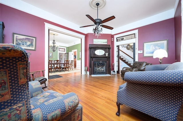 living area featuring a fireplace, wood finished floors, and ceiling fan with notable chandelier