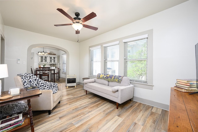 living area with light wood finished floors, baseboards, arched walkways, heating unit, and ceiling fan with notable chandelier