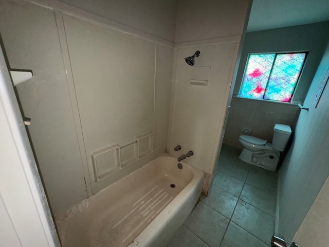 bathroom featuring toilet, tile patterned floors,  shower combination, and tile walls