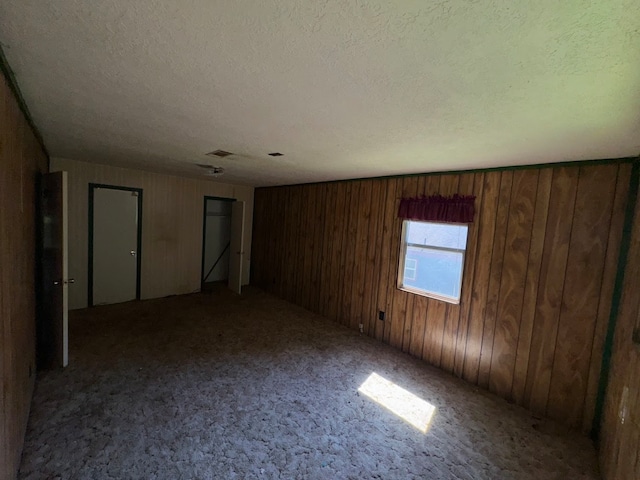 carpeted spare room featuring a textured ceiling and wooden walls