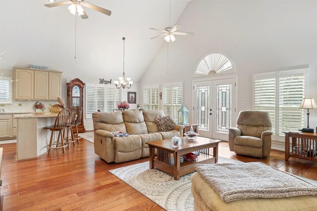 living room with ceiling fan with notable chandelier, high vaulted ceiling, a healthy amount of sunlight, and light hardwood / wood-style floors