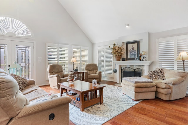 living room with a stone fireplace, light hardwood / wood-style floors, and high vaulted ceiling