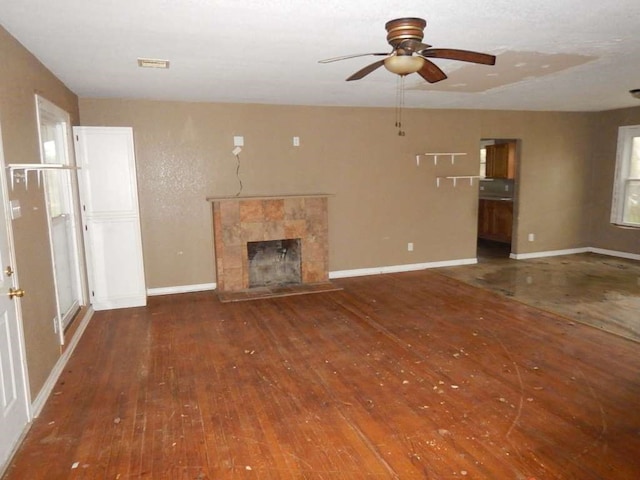 unfurnished living room featuring a tile fireplace, dark hardwood / wood-style flooring, and ceiling fan