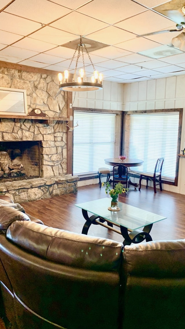 living room featuring a stone fireplace, hardwood / wood-style flooring, a healthy amount of sunlight, and a paneled ceiling