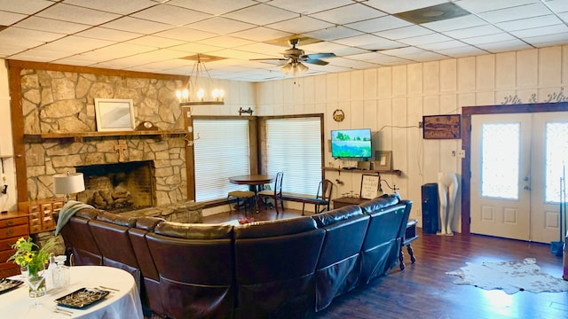 living room featuring a stone fireplace, wood-type flooring, ceiling fan with notable chandelier, and a paneled ceiling