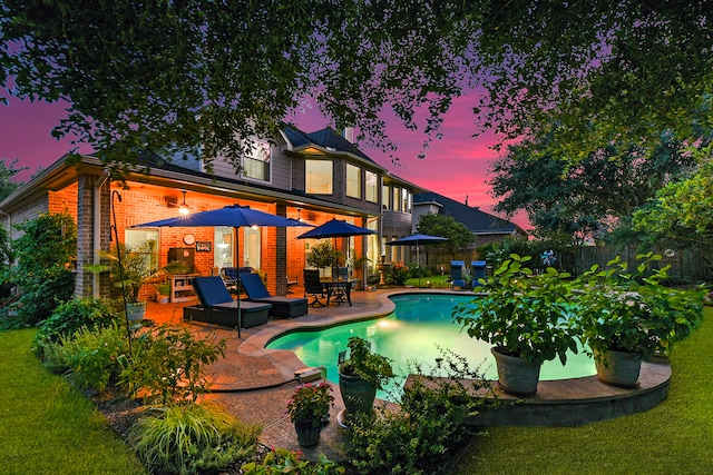 pool at dusk featuring a patio and a lawn