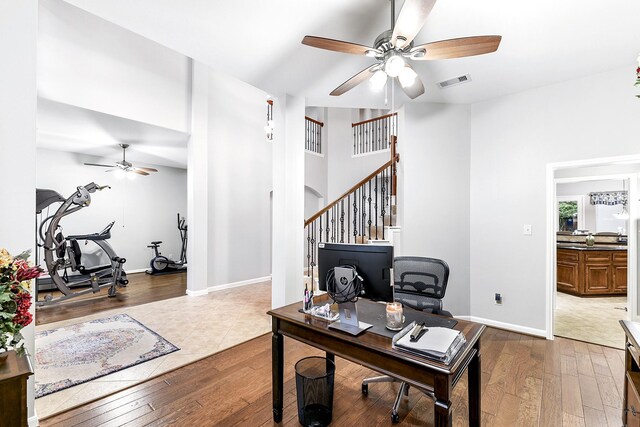 home office with ceiling fan, wood-type flooring, and a towering ceiling