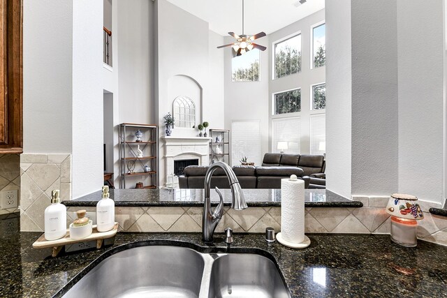 kitchen with dark stone counters, ceiling fan, tasteful backsplash, a high ceiling, and sink