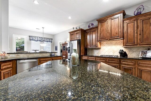 kitchen featuring dark stone counters, pendant lighting, backsplash, and stainless steel appliances